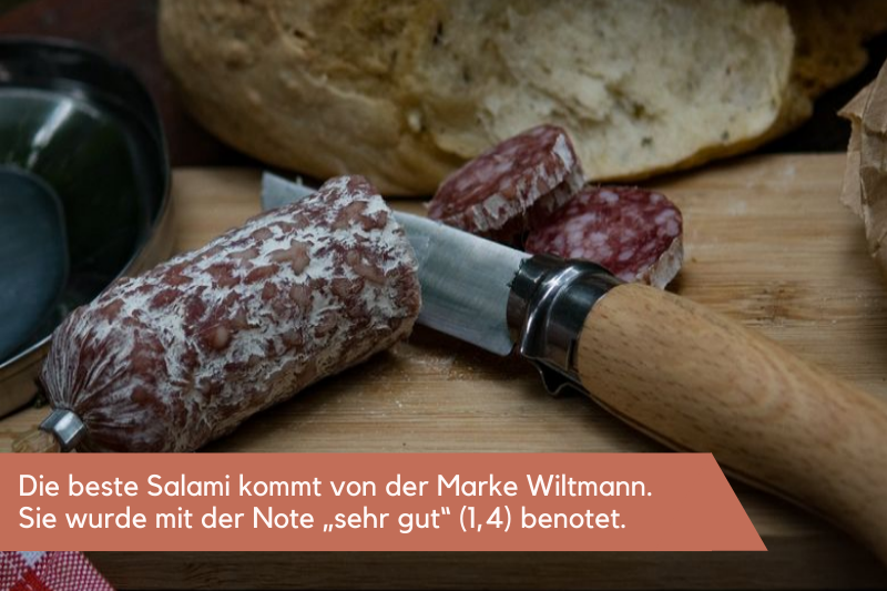 Salami wird auf einem Holzbrett mit Messer durchgeschnitten