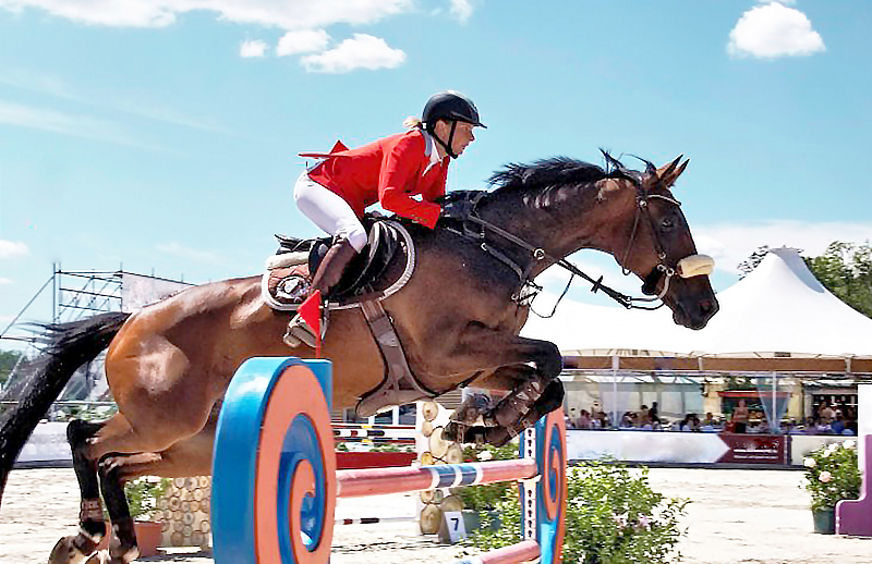 Fortgeschrittene Reiterin in hellrotem Turnierjacket beim Springen.