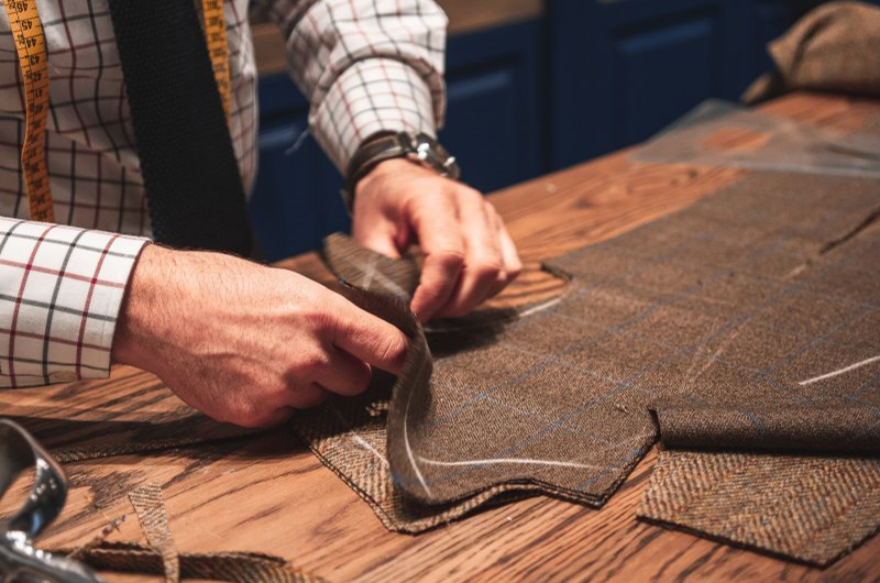 Schneider an einem Zuschneidetisch sortiert Turnierjackeet-Teile